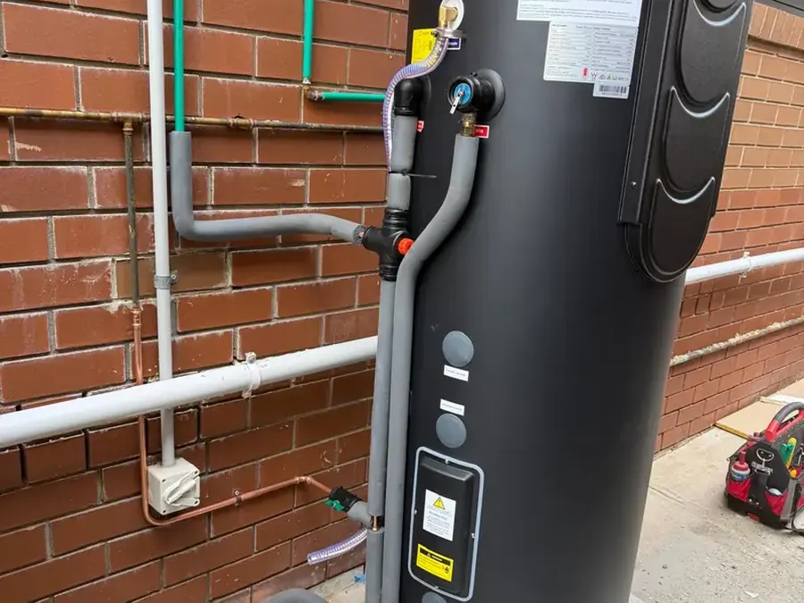Heat pump hot water unit installed against a brick wall